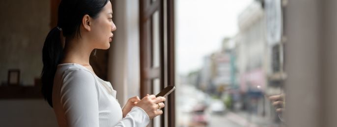 A young woman looking thoughtfully out of a window in natural light.