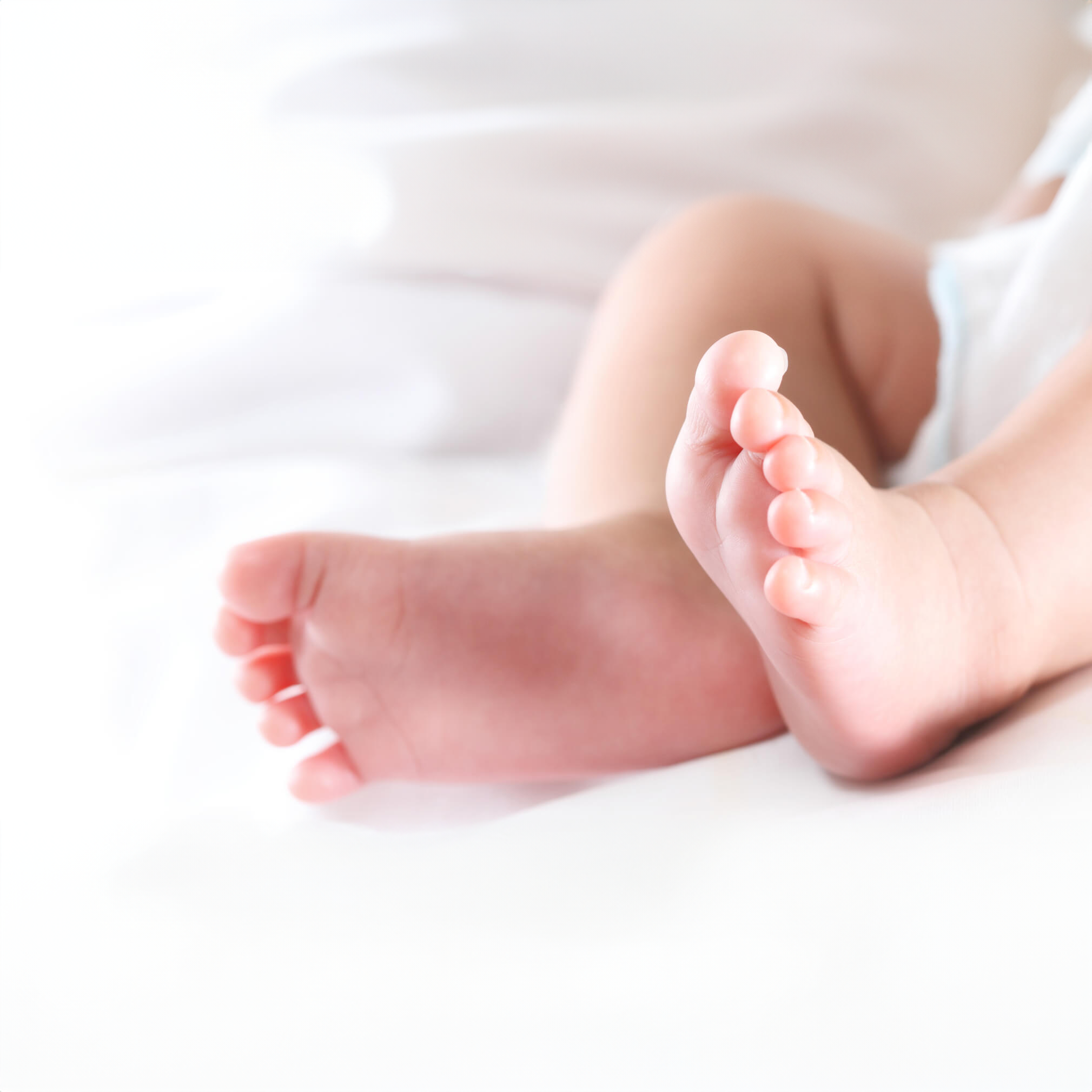 新生婴儿的脚部特写，静静地放在柔软的白色表面上，象征纯真、温暖和生命的开始。