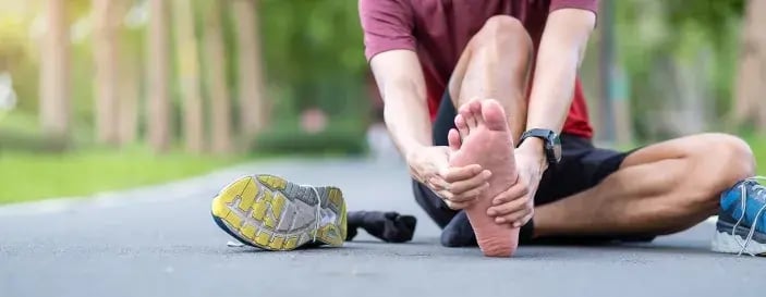 Runner sitting on pavement holding his foot in pain, showing signs of plantar fasciitis after exercise.