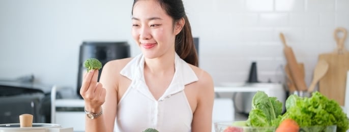 Asian woman choosing broccoli while preparing a healthy meal, promoting a balanced lifestyle.
