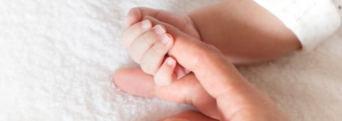 Baby holding an adult’s finger, representing secure attachment and emotional development during the first three years of life.