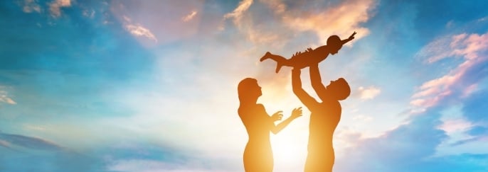 Parents lifting their baby into the air, symbolising emotional bonding and a sense of security in early childhood.