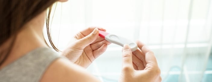 Woman holding a pregnancy test with a hopeful expression, representing conception and early pregnancy detection