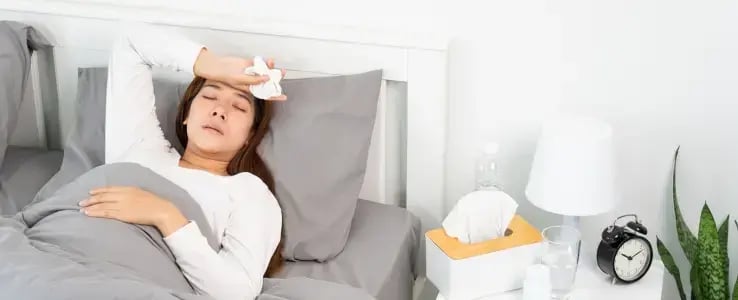 Woman resting in bed with a cloth on her forehead, illustrating fever symptoms.