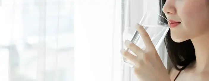 女性飲用清水，示意保持充足水分有助泌尿道健康。