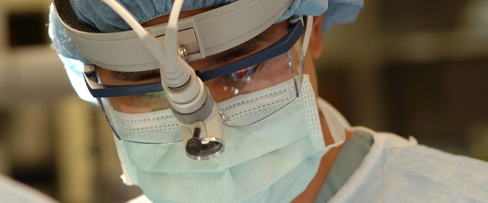 doctor operating on a patient, while wearing magnifying glasses