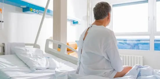 male patient sitting on bed looking at window
