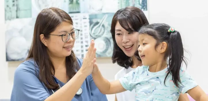 doctor high fiving child, with mother looking on